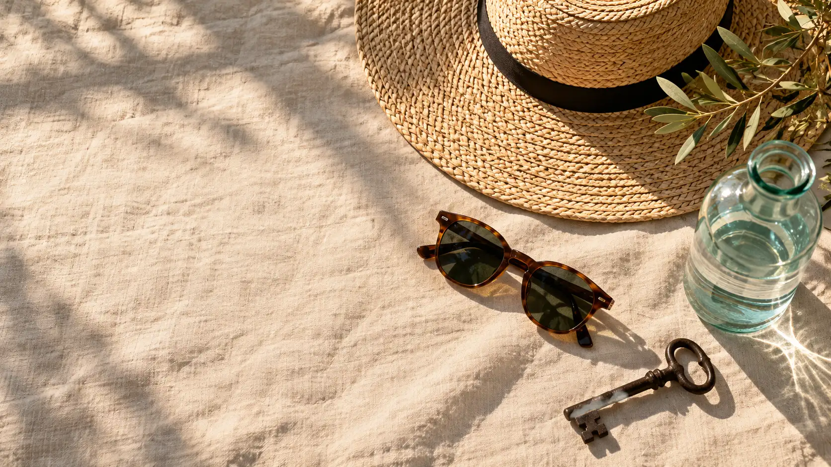 Sombrero de paja, gafas de sol, botella de agua de cristal y una llave antigua sobre lino